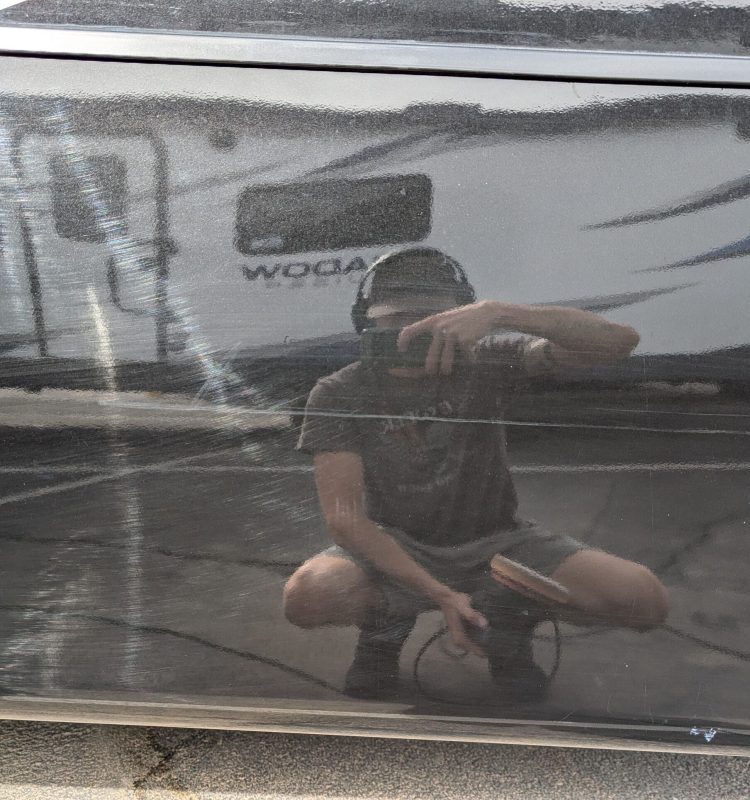 a professional detailer taking a picture of himself in the reflective paint before doing a correction
